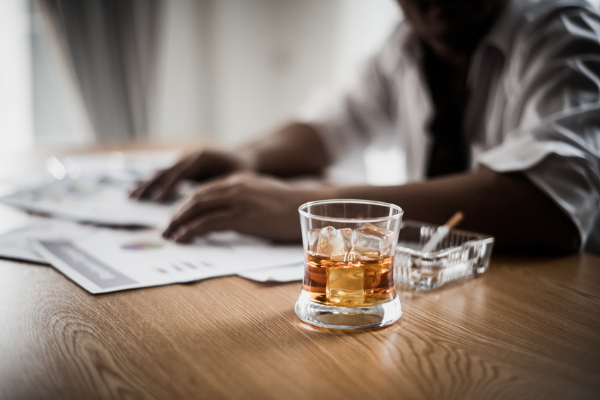 un salarié à son bureau, près de lui un verre d'alcool, un cendrier et une cigarette allumée